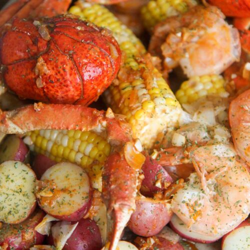 cooked lobster tails, corn, potatoes, sausage, crab legs, and shrimp, with sauce and parsley on top.
