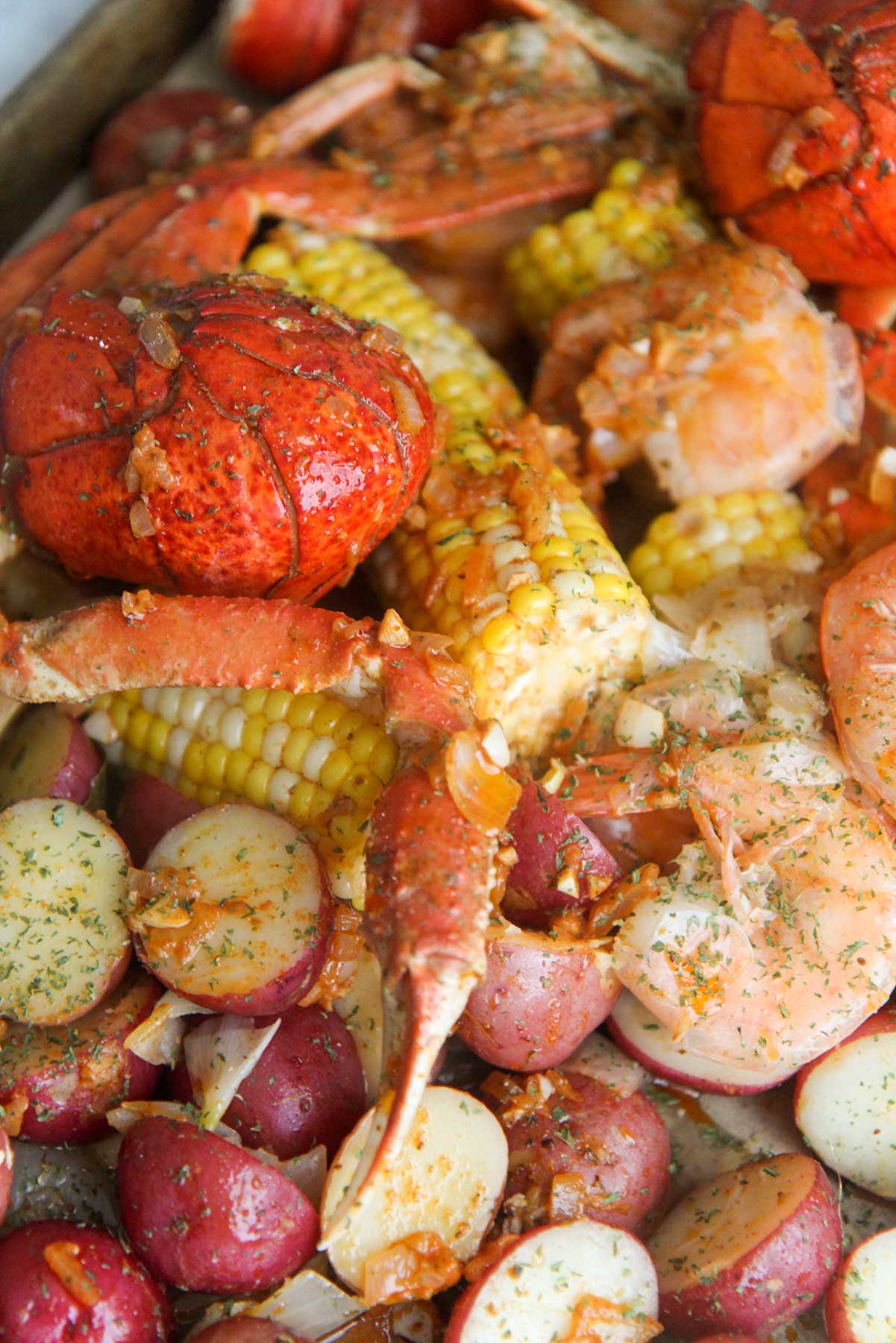 cooked lobster tails, corn, potatoes, sausage, crab legs, and shrimp, with sauce and parsley on top. 