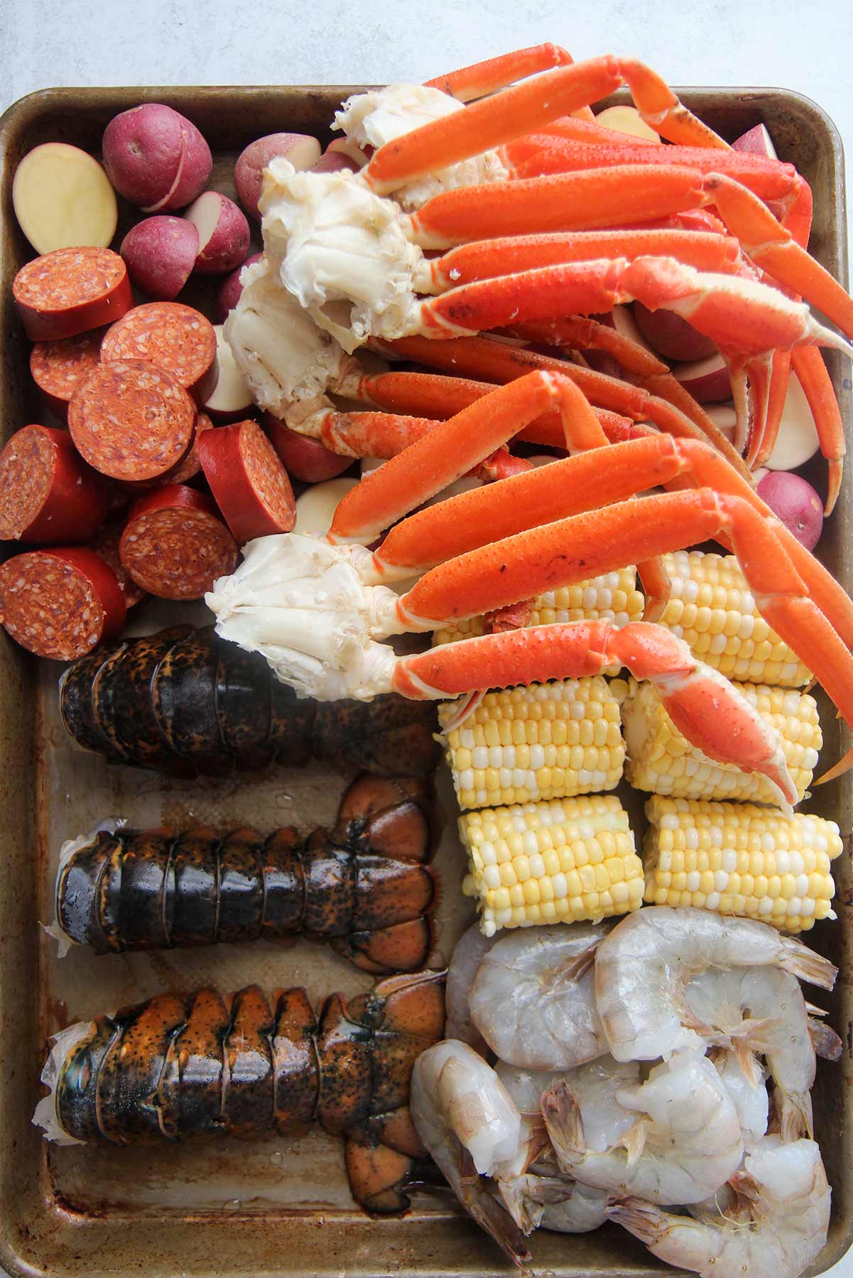 ingredients for seafood boil. Raw shellfish, corn, potatoes, and sausage.