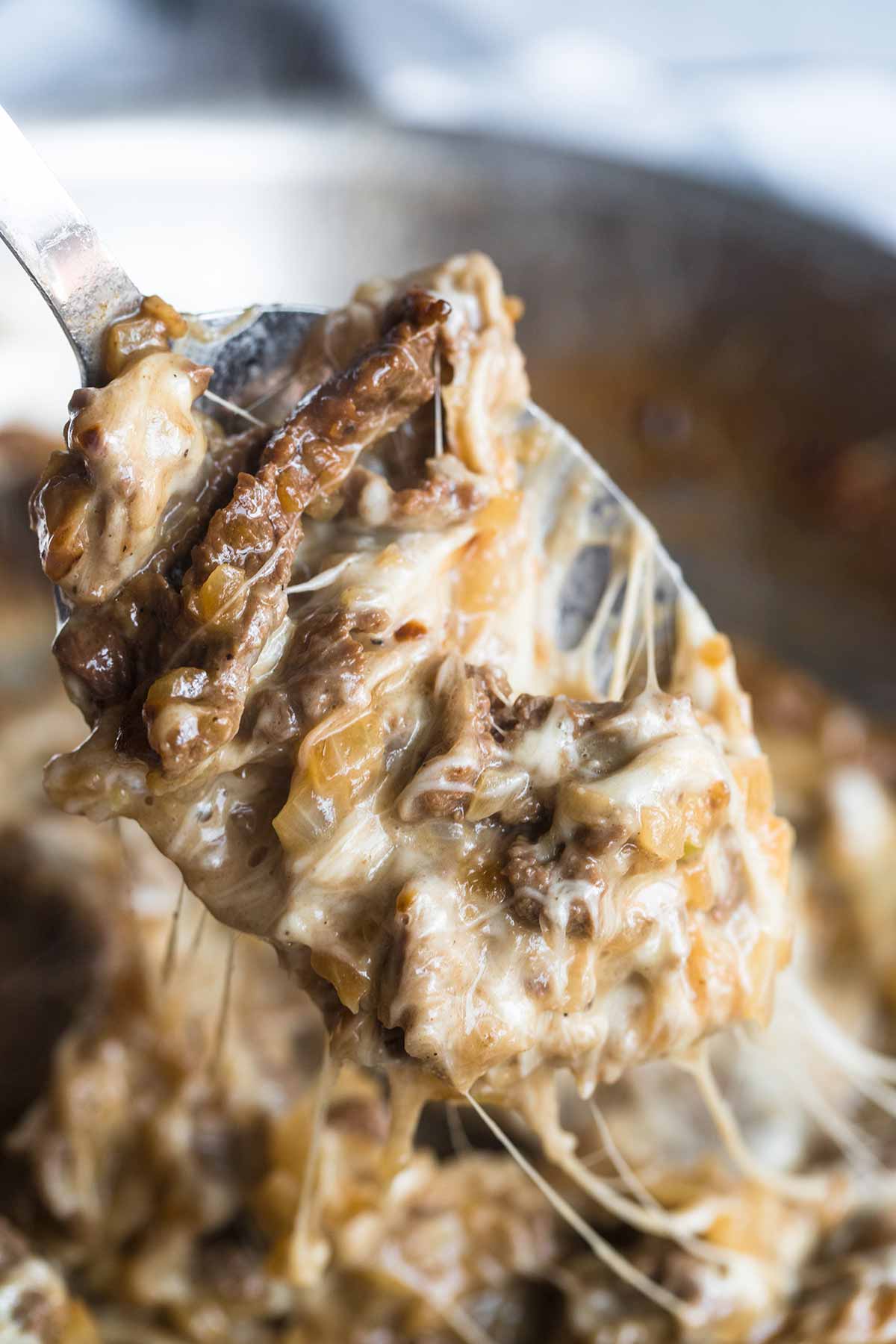 a spoon filled with beef, cheese, and onions. 