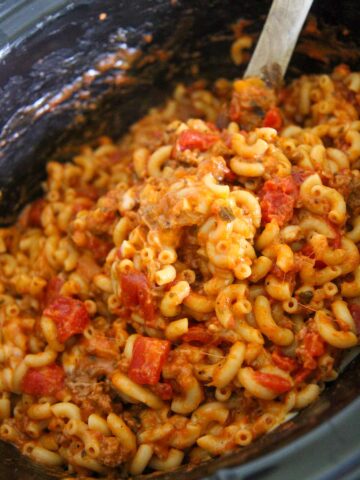 crockpot cheesy beef goulash with a wooden spoon.