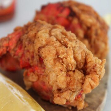 Two fried lobster tails up close with a lemon wedge on the side.