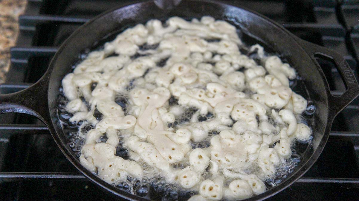 funnel cake frying in a cast-iron skillet on the stovetop. 