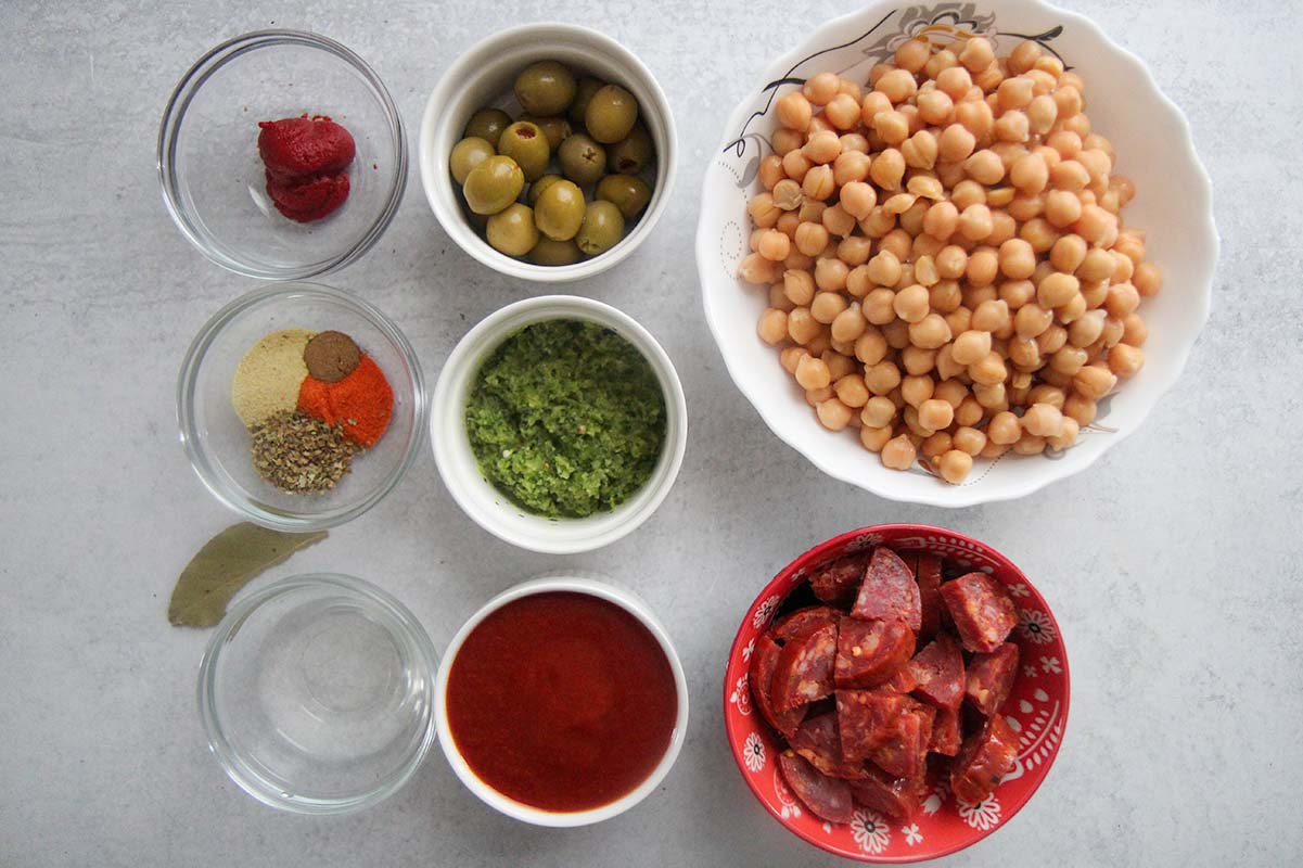 chickpeas, olives, spices, tomato sauce, tomato paste, sofrito, and chorizo in small bowls. 