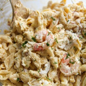 seafood pasta salad in a glass bowl with a wooden spoon.