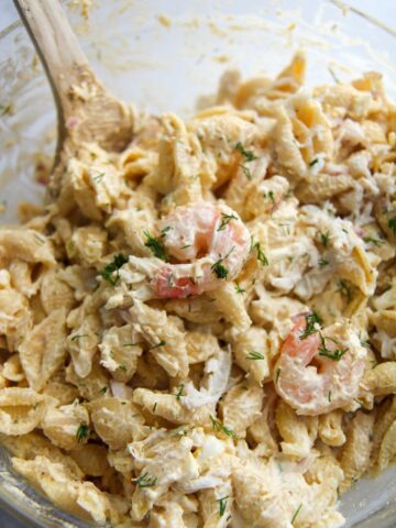 seafood pasta salad in a glass bowl with a wooden spoon.