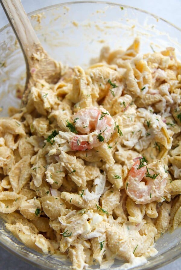 seafood pasta salad in a glass bowl with a wooden spoon.