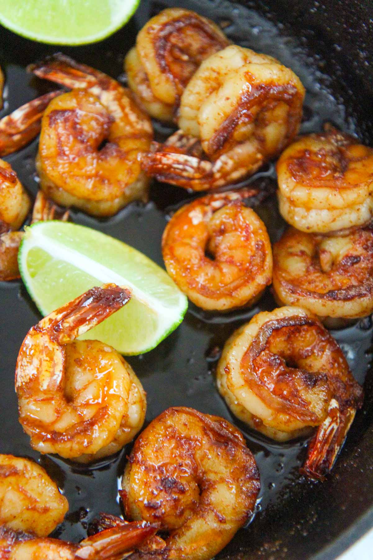 cooked shrimp in a skillet with lime wedges. 