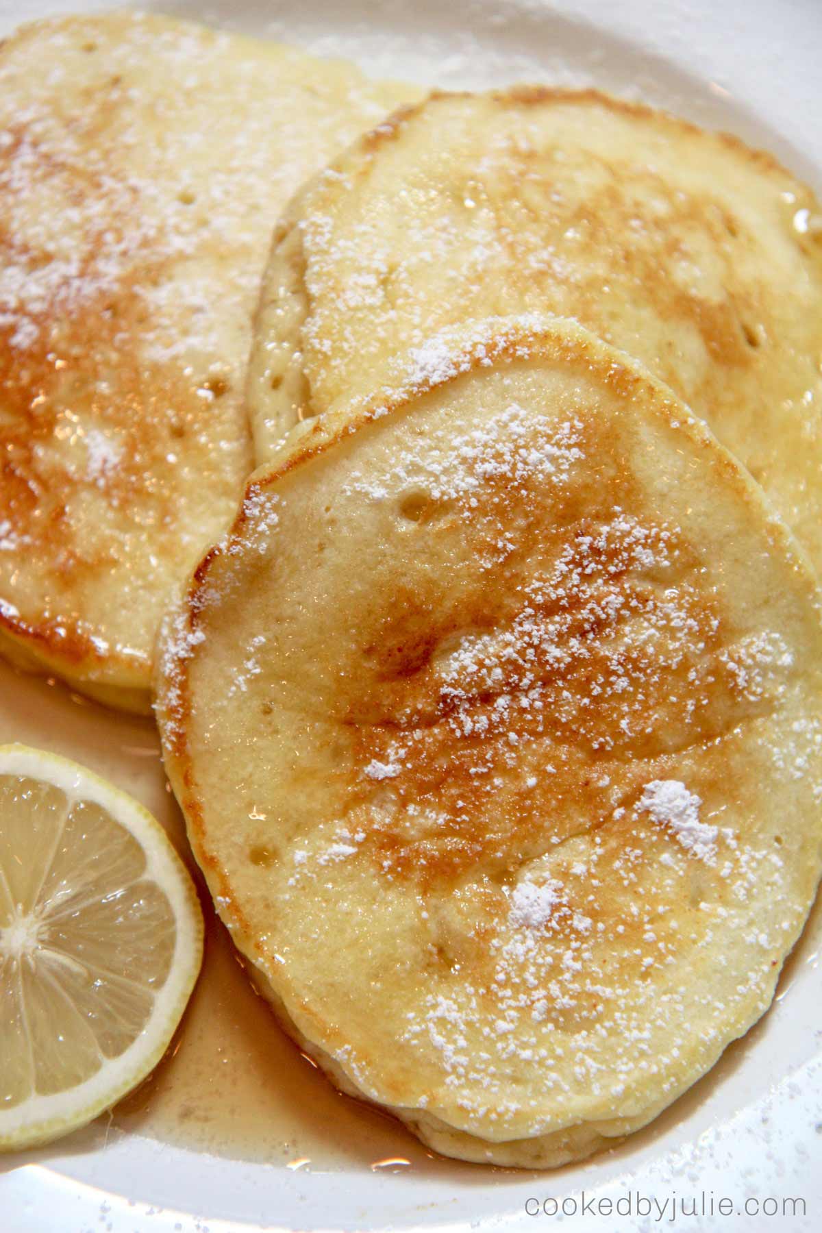 three lemon ricotta pancakes with powdered sugar on top and a lemon slice. 