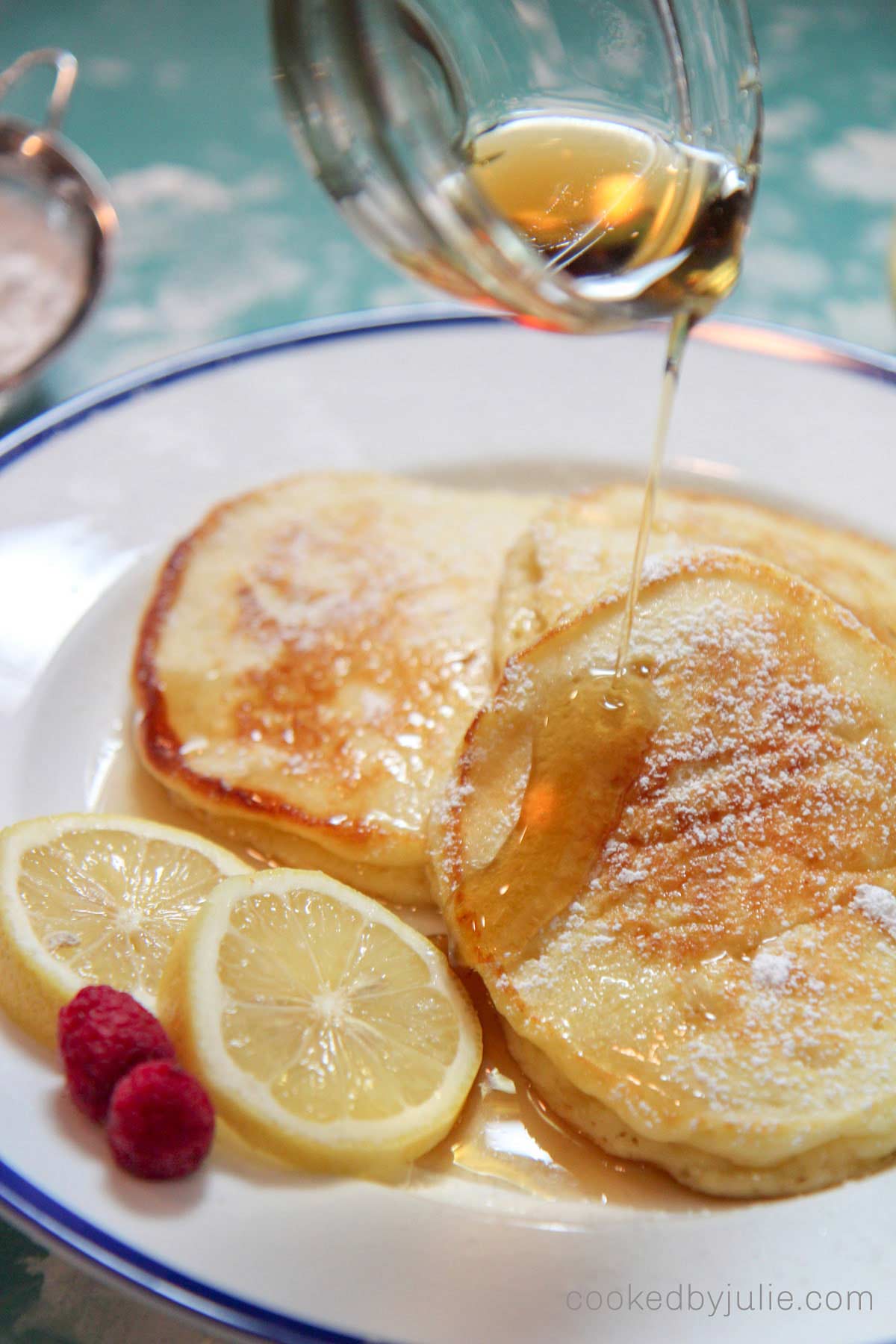 lemon ricotta pancakes with syrup, raspberries, and lemon slices. 