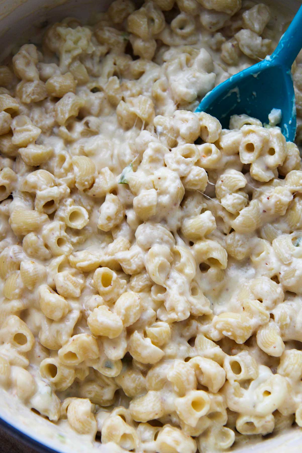 creamy spicy macaroni and cheese in a large pot with a blue spoon. 