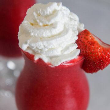 Strawberry daiquiri in a glass with whipped cream and a fresh strawberry.