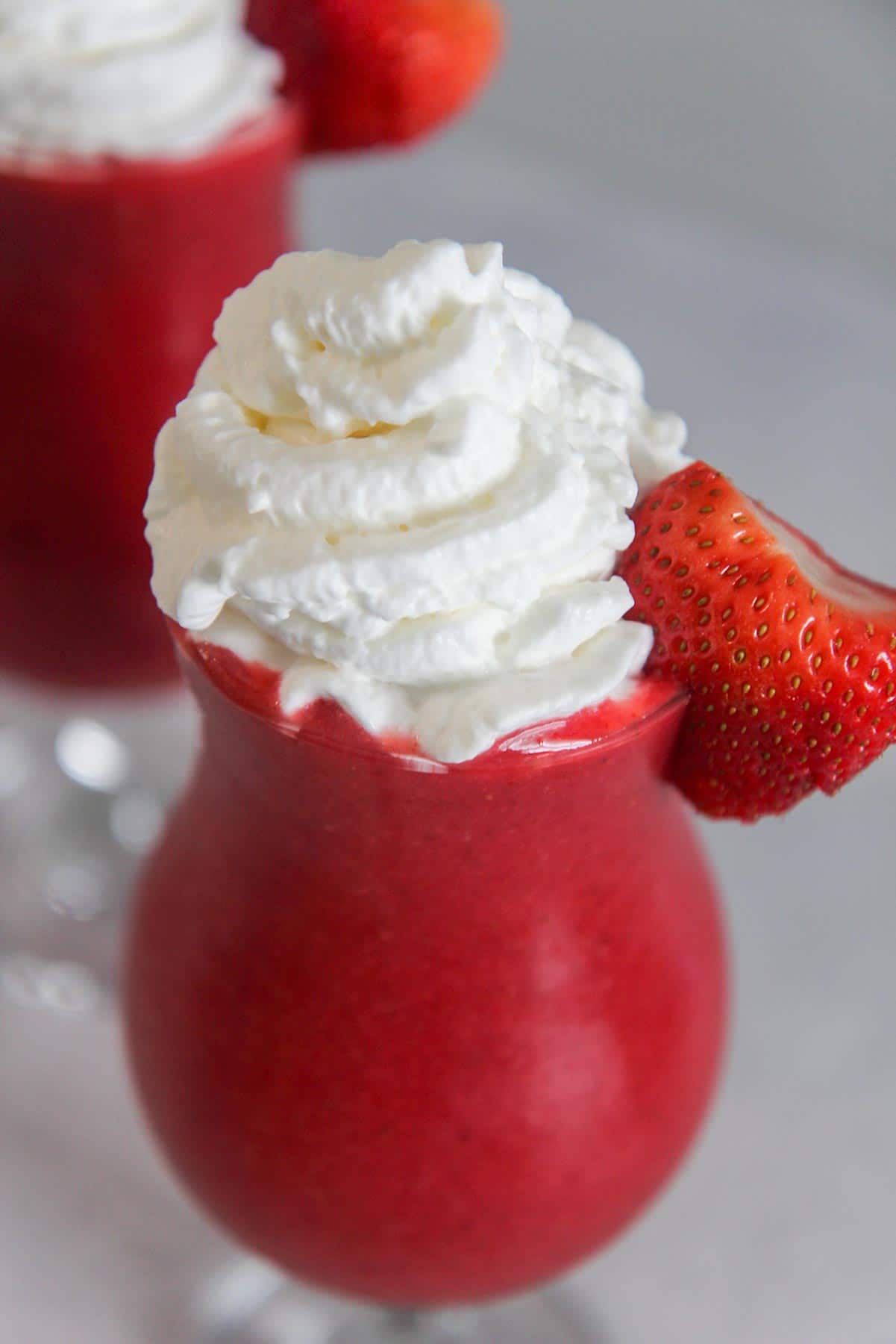 strawberry daiquiri in a glass with whipped cream on top and a fresh strawberry on the side. 