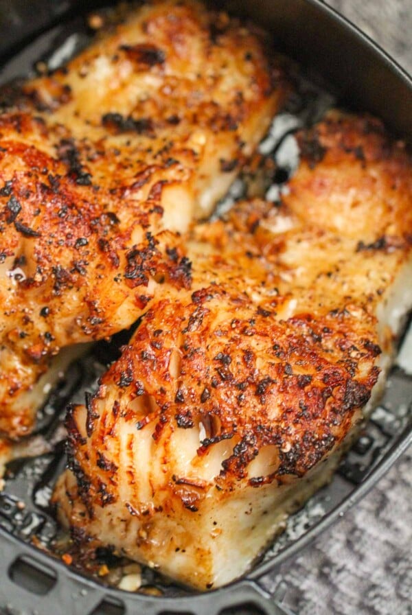 two cooked Chilean sea bass fillets in an air fryer basket.
