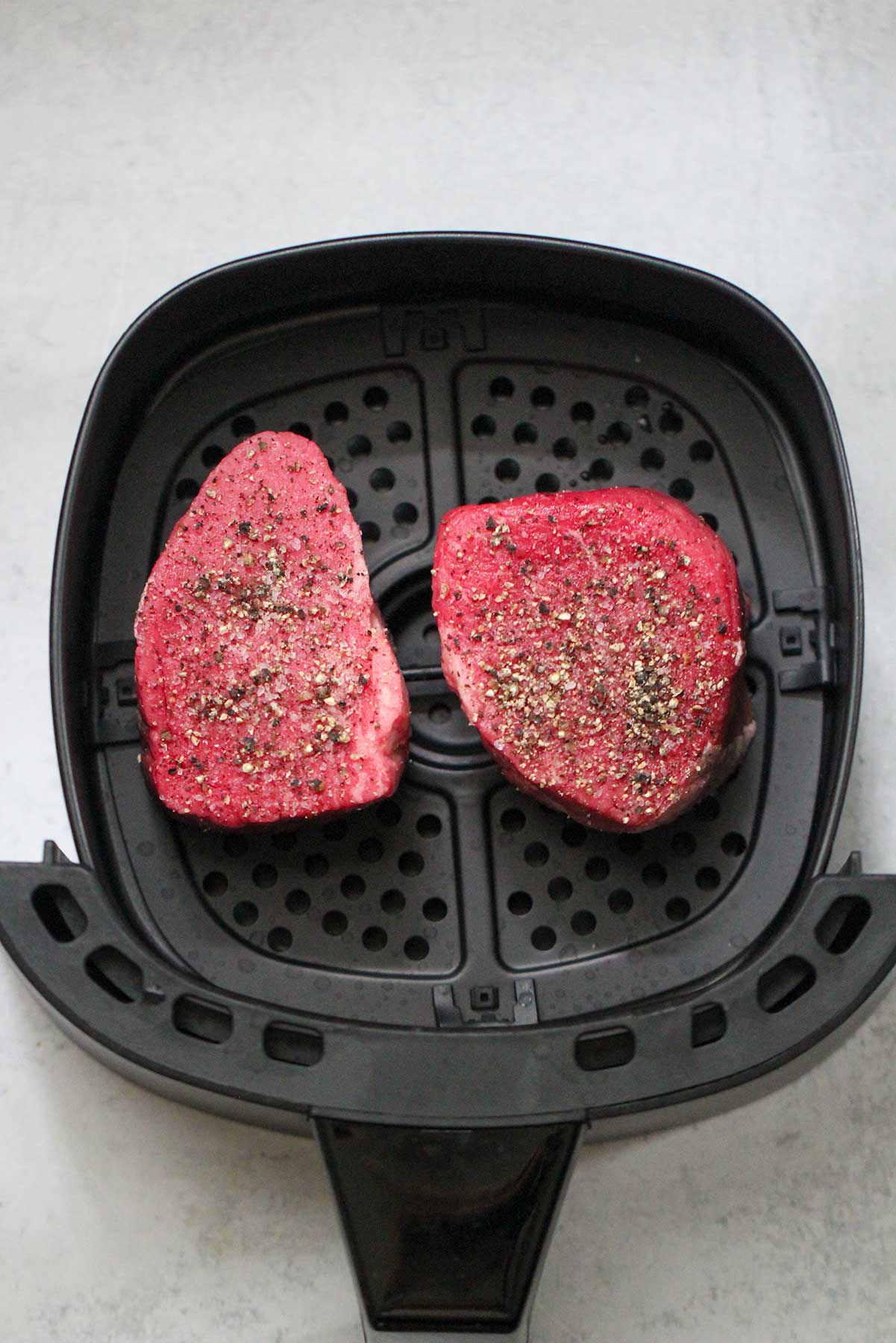 two raw filet mignon steaks in an air fryer basket.