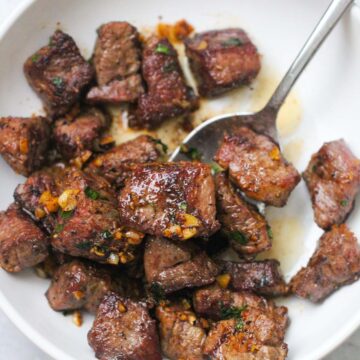 garlic butter steak tips on a white plate with a spoon.