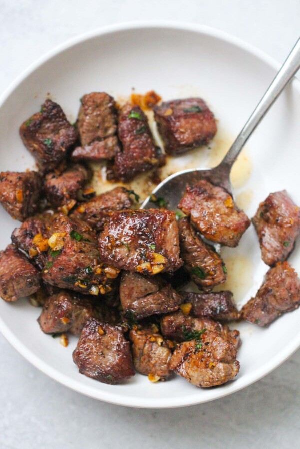 garlic butter steak tips on a white plate with a spoon.