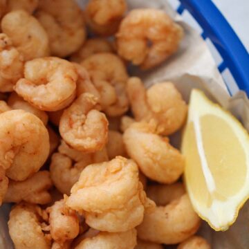 popcorn shrimp in a blue basket with a lemon wedge on the side.