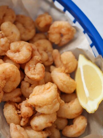 popcorn shrimp in a blue basket with a lemon wedge on the side.