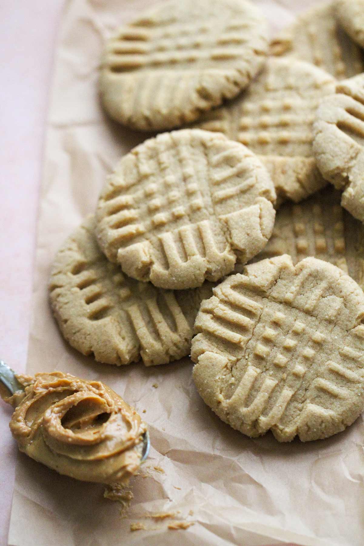 peanut butter cookies on top of parchment paper with a spoonful of peanut butter on the side. 