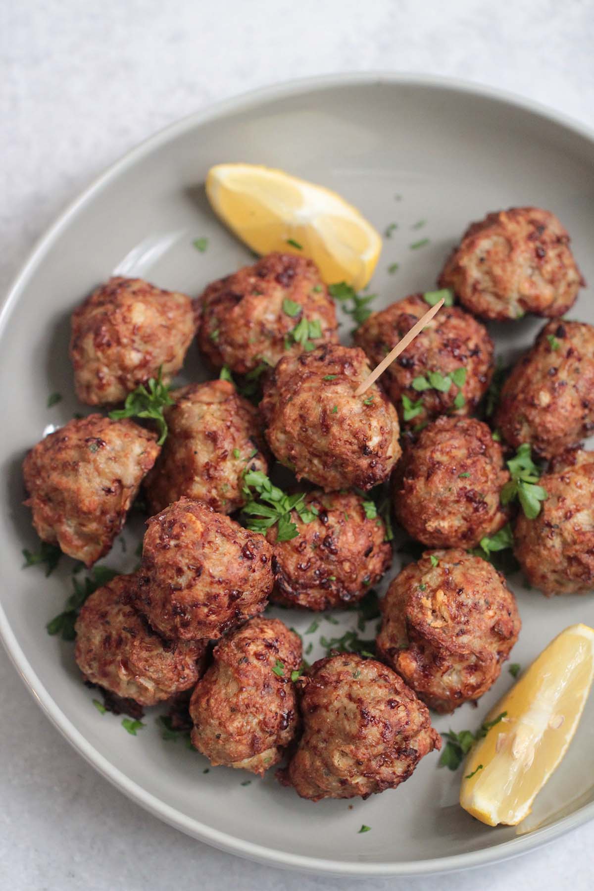 cooked air fryer turkey meatballs on a gray plate with lemon wedges and parsley. 