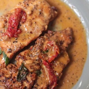 two cooked chicken breasts with cream sauce on a gray plate.