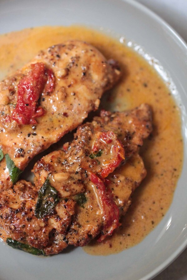 two cooked chicken breasts with cream sauce on a gray plate.