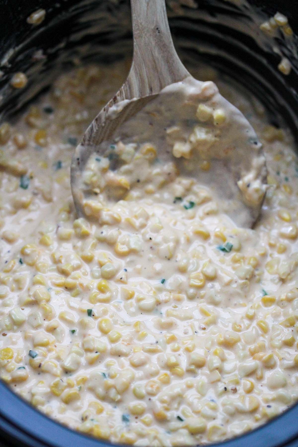 slow cooker creamed corn with a wooden spoon.