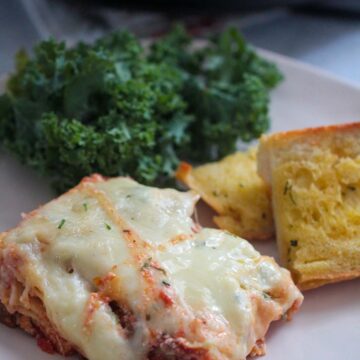 a slice of lasagna with garlic bread and kale salad on the side.