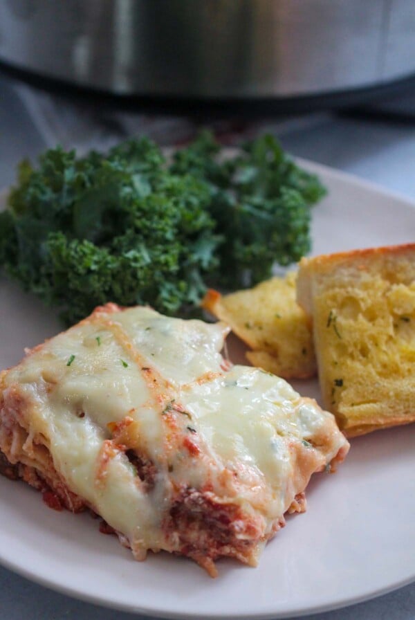 a slice of lasagna with garlic bread and kale salad on the side.