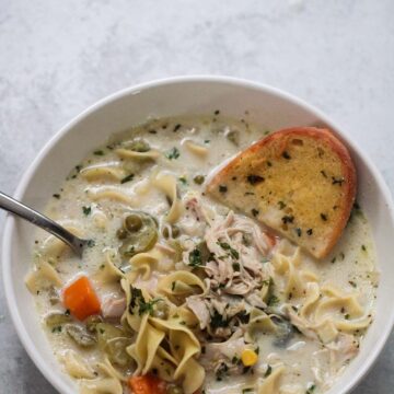 creamy chicken noodle soup in a bowl with a spoon and slice of garlic bread.