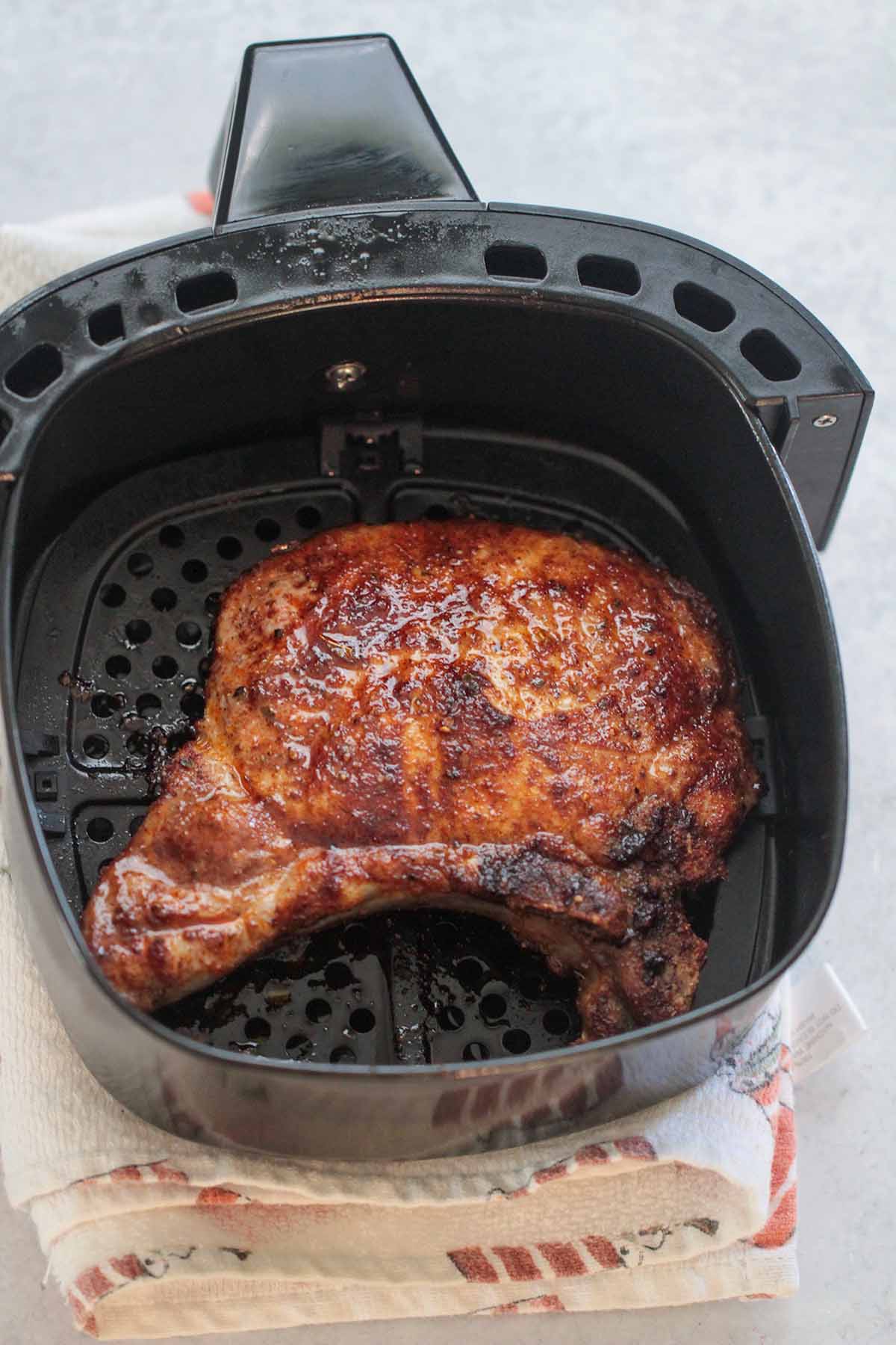 one cooked pork chop in the air fryer basket. 