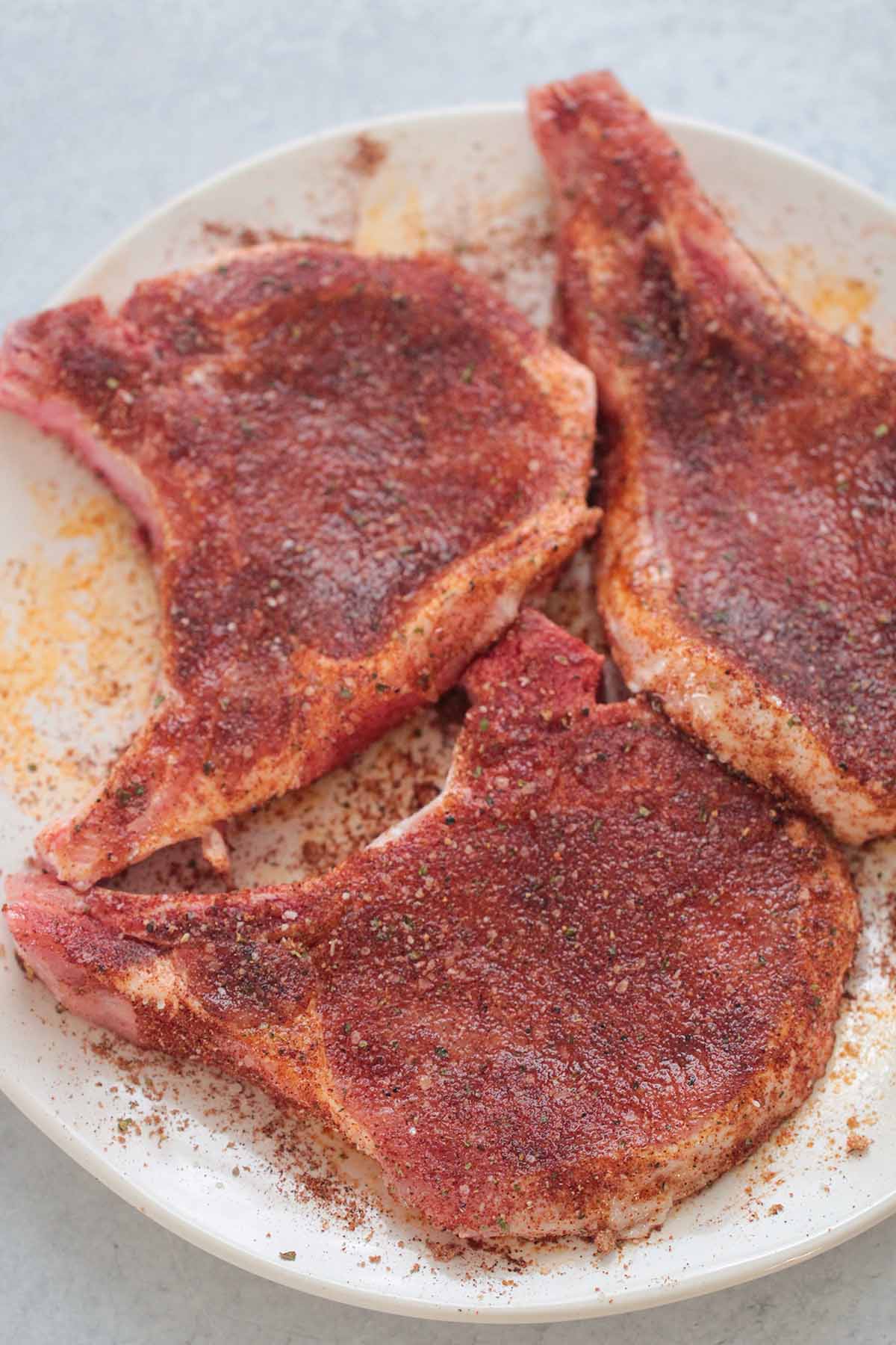 raw seasoned pork chops on a plate. 