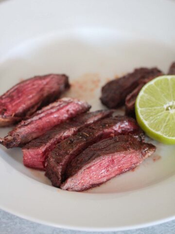 air fryer carne asada on a white plate with lime on the side.