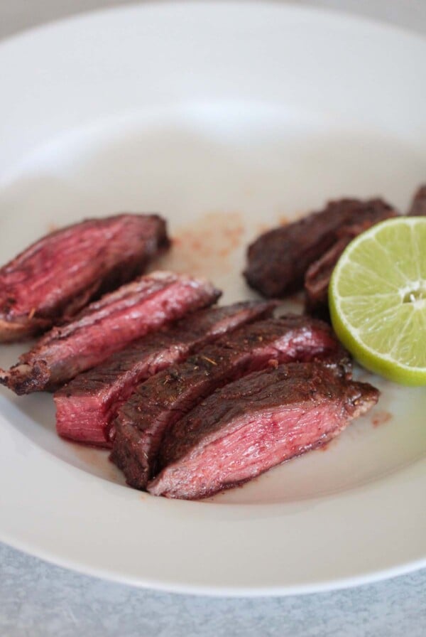 air fryer carne asada on a white plate with lime on the side.
