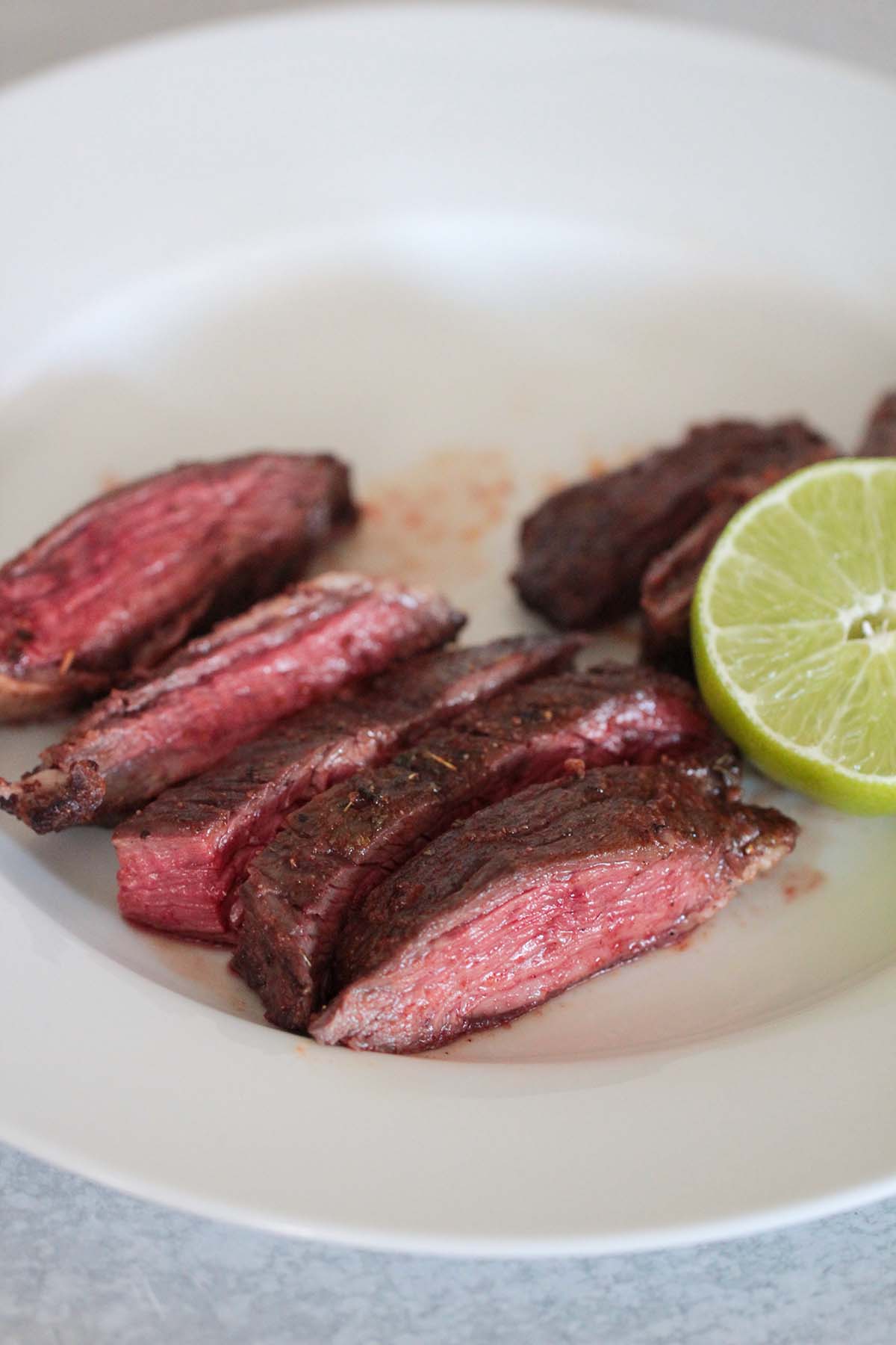 air fryer carne asada on a white plate with lime on the side. 