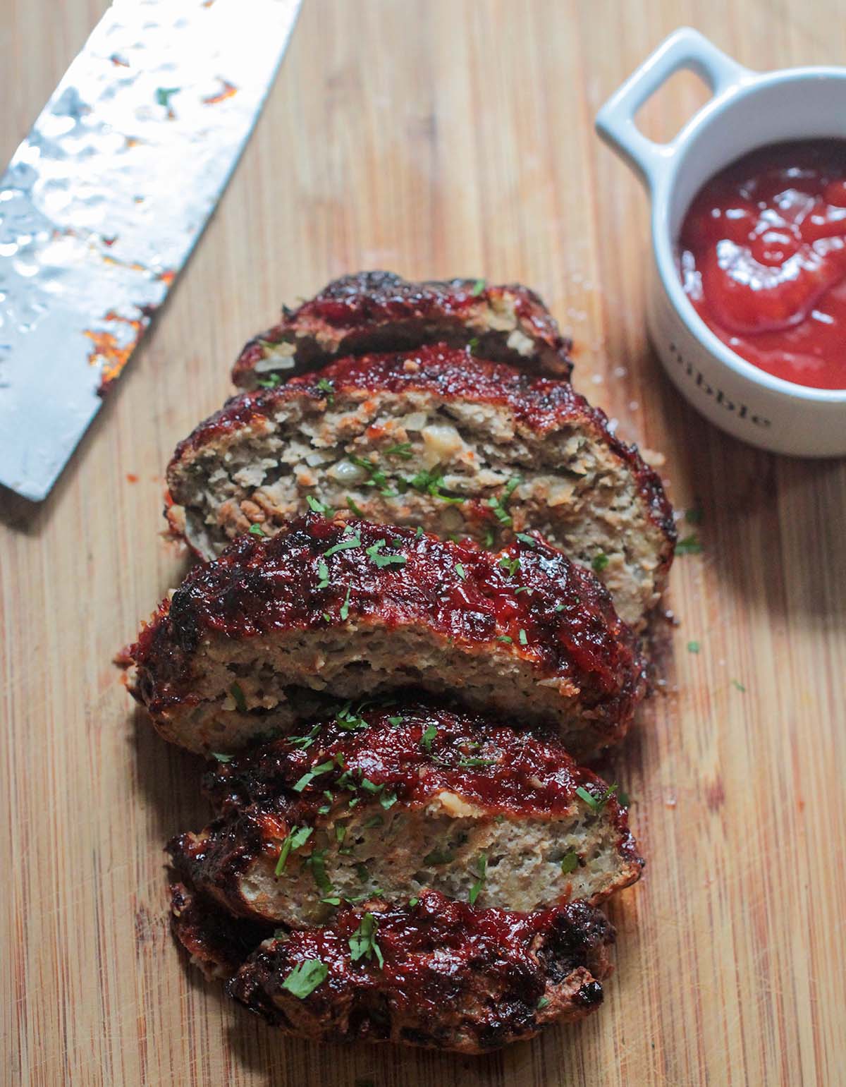 sliced meatloaf on a wooden board with a knife and ketchup on the side. 