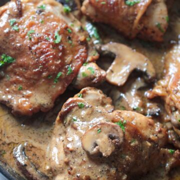 champagne chicken in a skillet with cream sauce, mushrooms, and parsley.