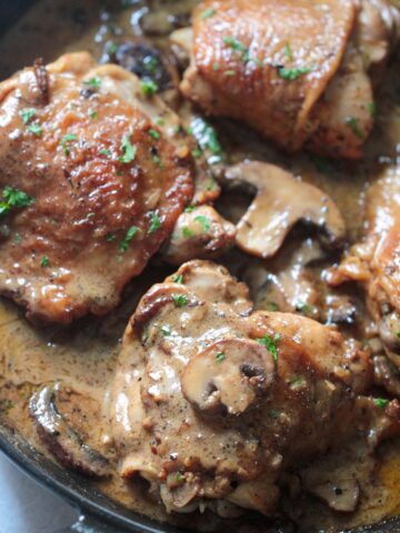 champagne chicken in a skillet with cream sauce, mushrooms, and parsley.