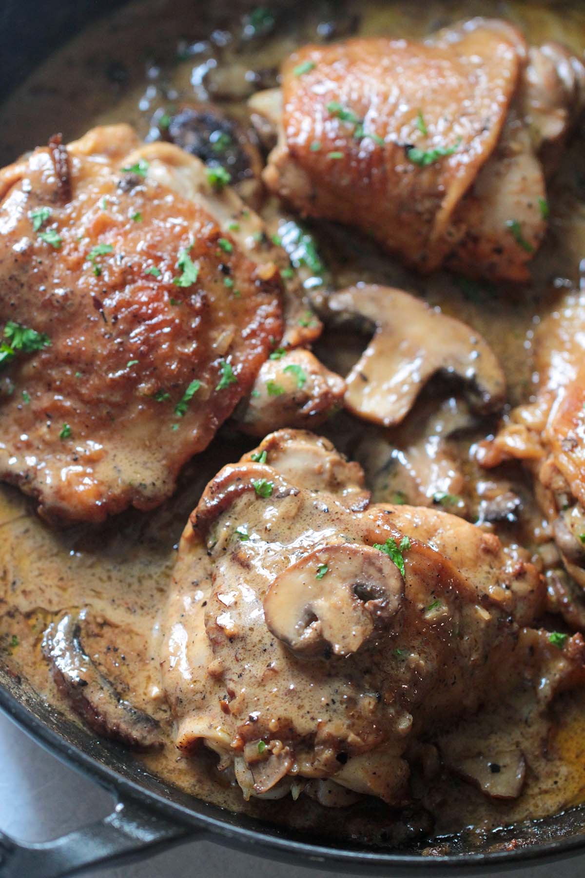 champagne chicken in a skillet with cream sauce, mushrooms, and parsley. 