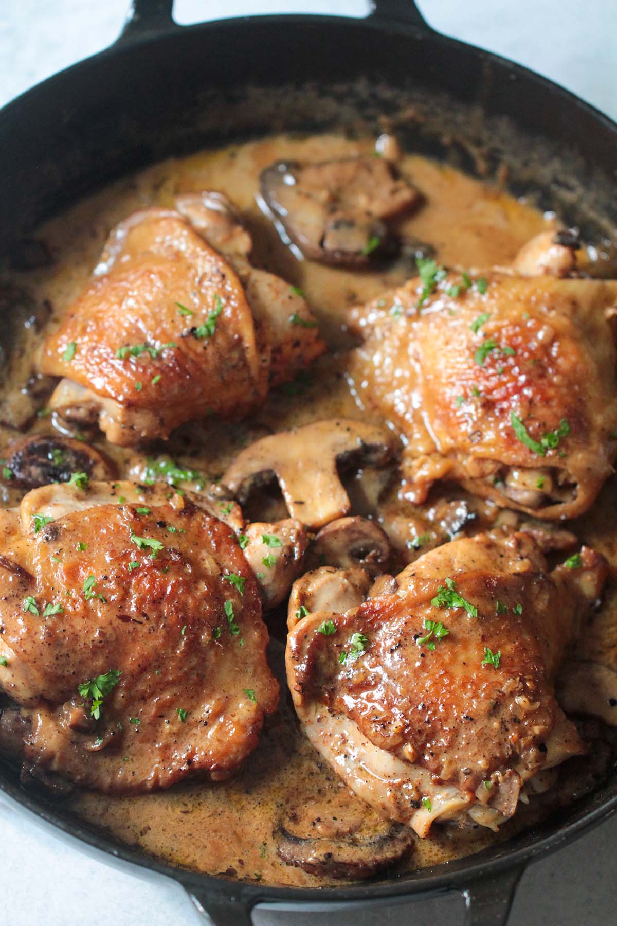 four chicken thighs in a skillet with sauce. 