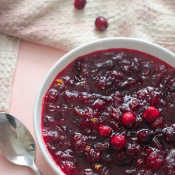 classic cranberry sauce in a bowl with a spoon, towel, and cranberries on the side.