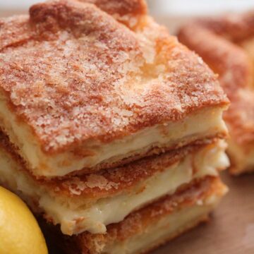 three lemon cream cheese bars stacked on a wooden board with a lemon on the side.