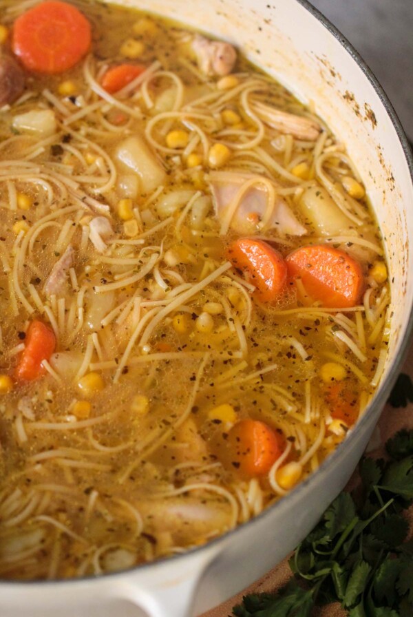 sopa de pollo in a white pot with cilantro on the side.