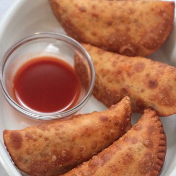 Four spicy beef and cheese empanadas with hot sauce on the side.
