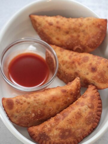 Four spicy beef and cheese empanadas with hot sauce on the side.