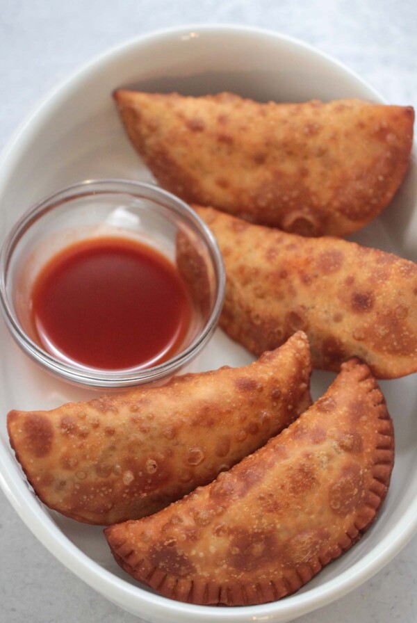 Four spicy beef and cheese empanadas with hot sauce on the side.