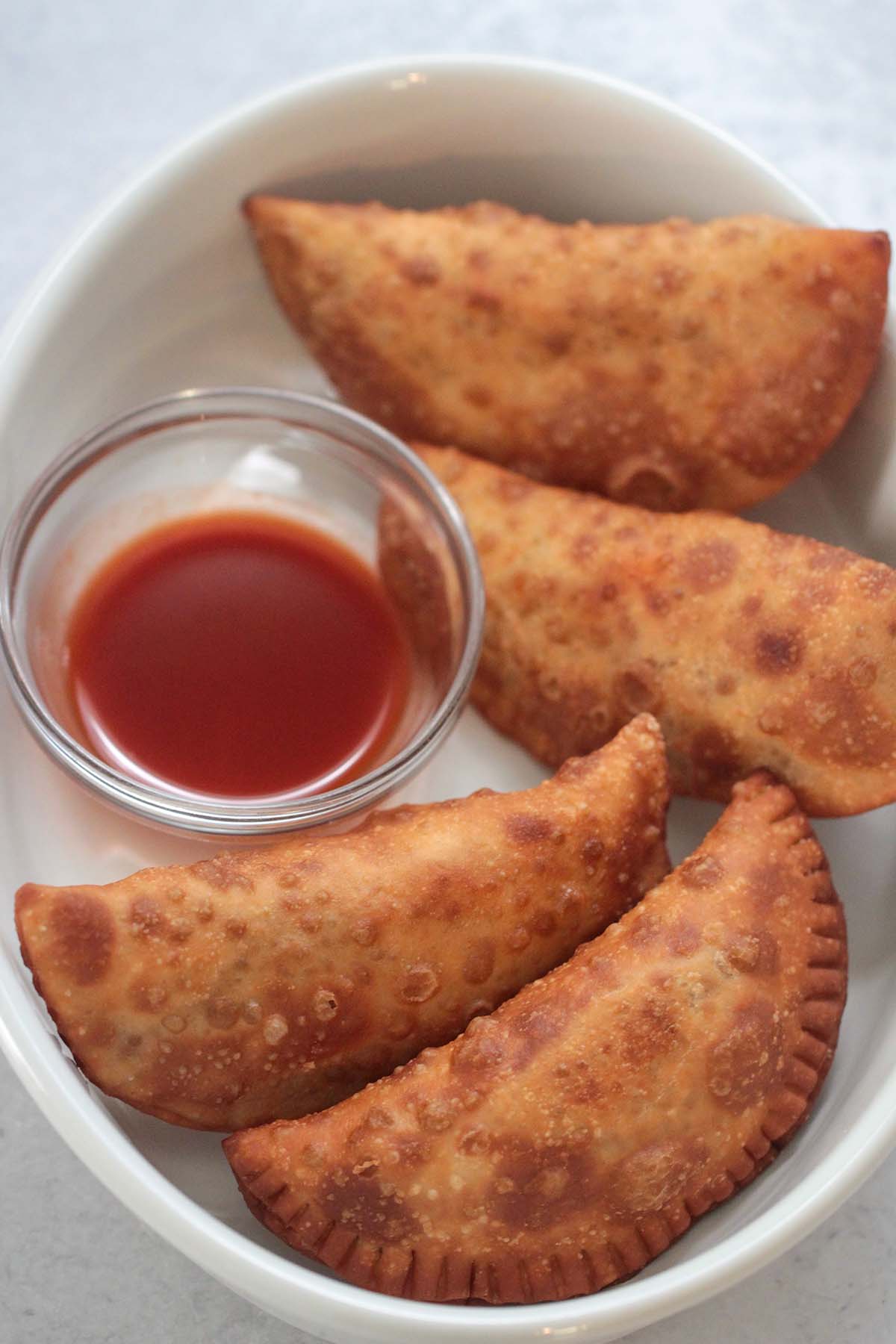 Four spicy beef and cheese empanadas with hot sauce on the side. 