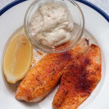 air fryer tilapia with tartar sauce and a lemon wedge.