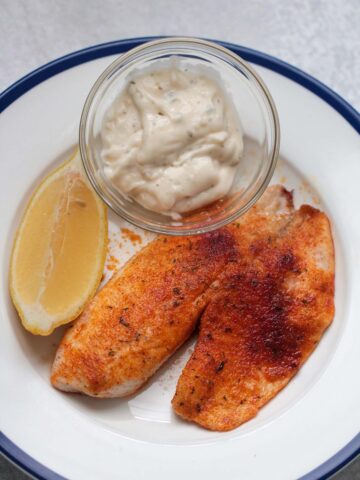 air fryer tilapia with tartar sauce and a lemon wedge.